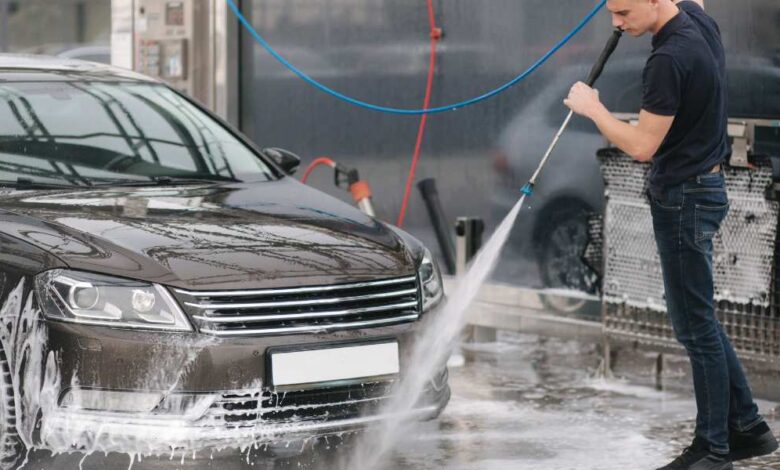 a man in dark blue shirt and jeans pant using cordless pressure to clean black car.