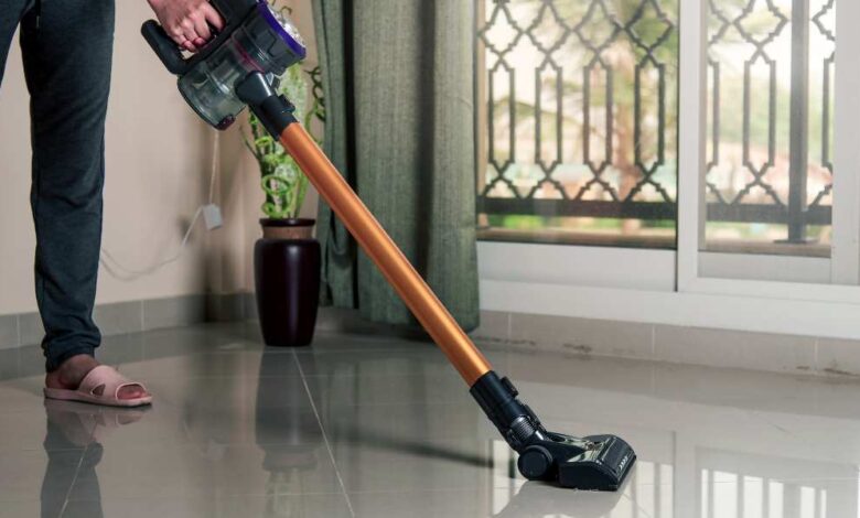 a man in balck pant and gry sanddle using cordless stick vacuum on a white floor.